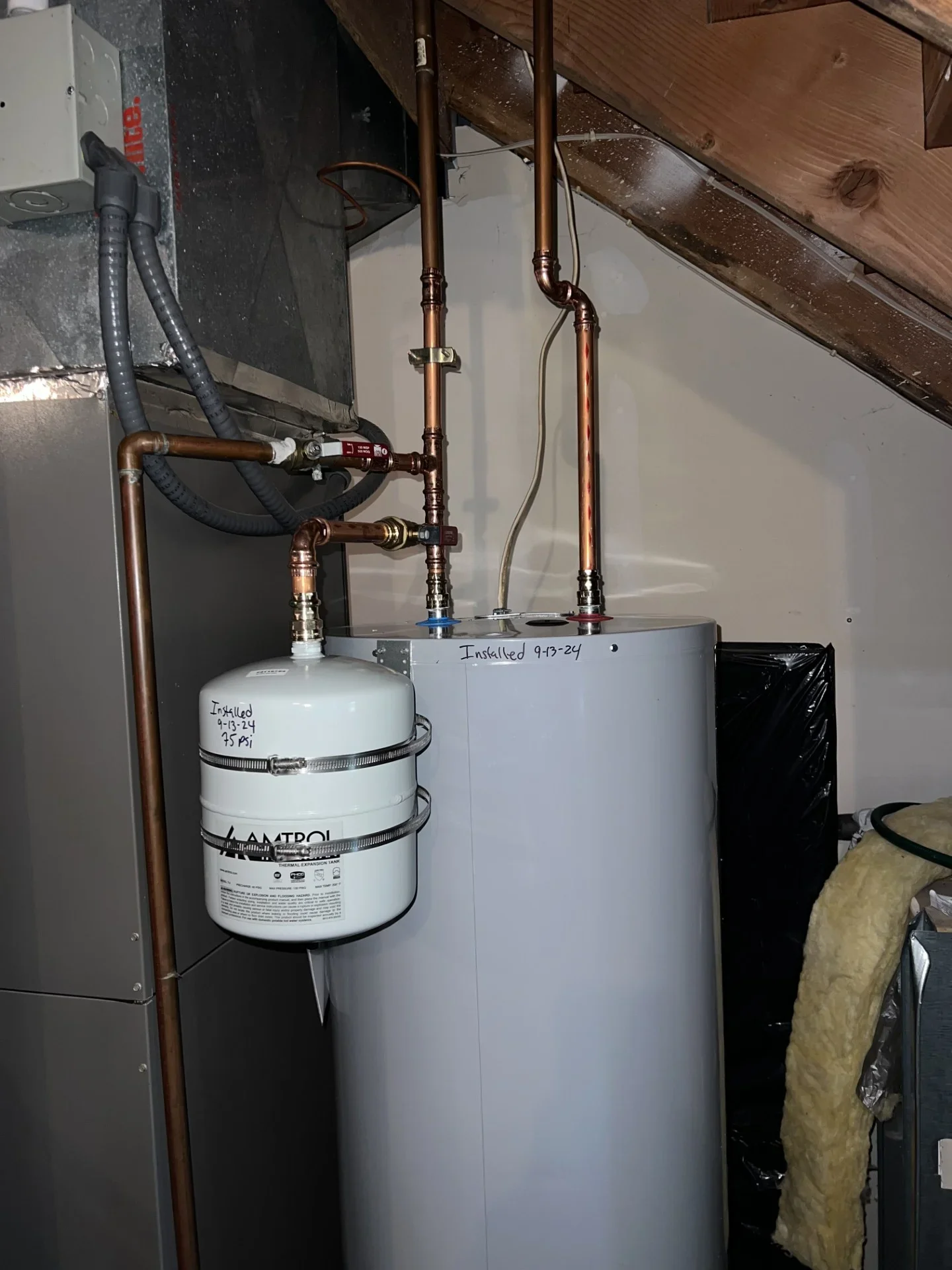 Water heater with Amtrol thermal expansion tank, copper piping, and red-handled shutoff valves installed in attic space