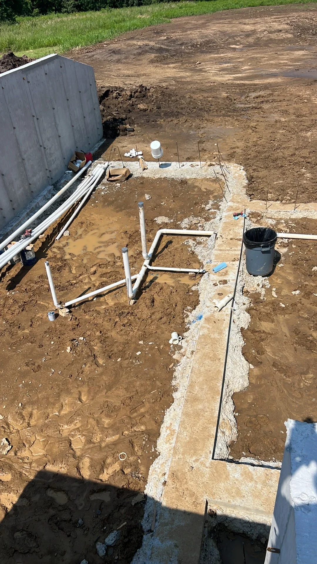 Underground PVC rough-in plumbing with vertical stub-outs over a concrete footing and foundation wall