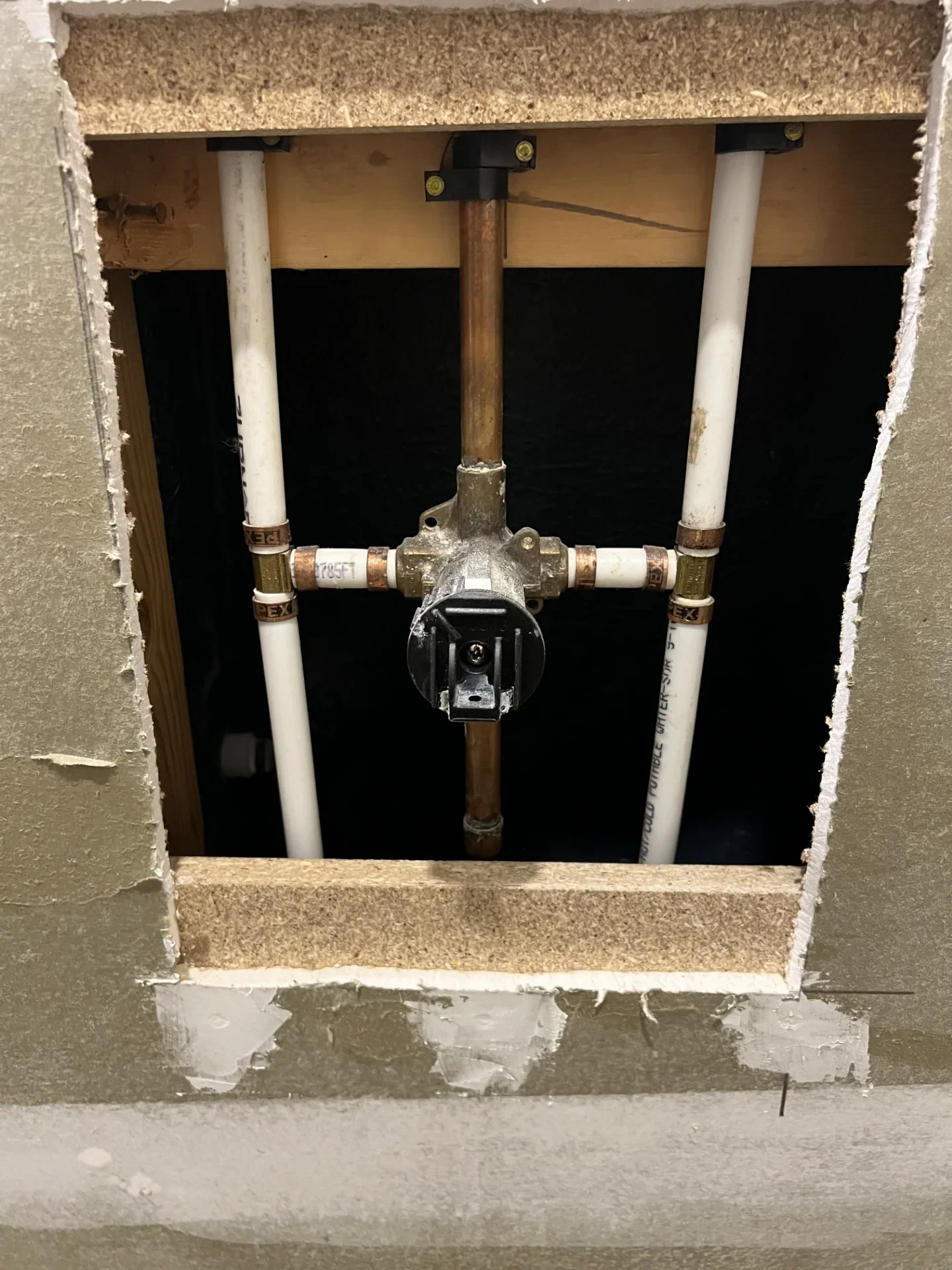 Shower valve rough-in with brass valve body, copper riser, and white PEX lines secured with crimp fittings in open wall framing