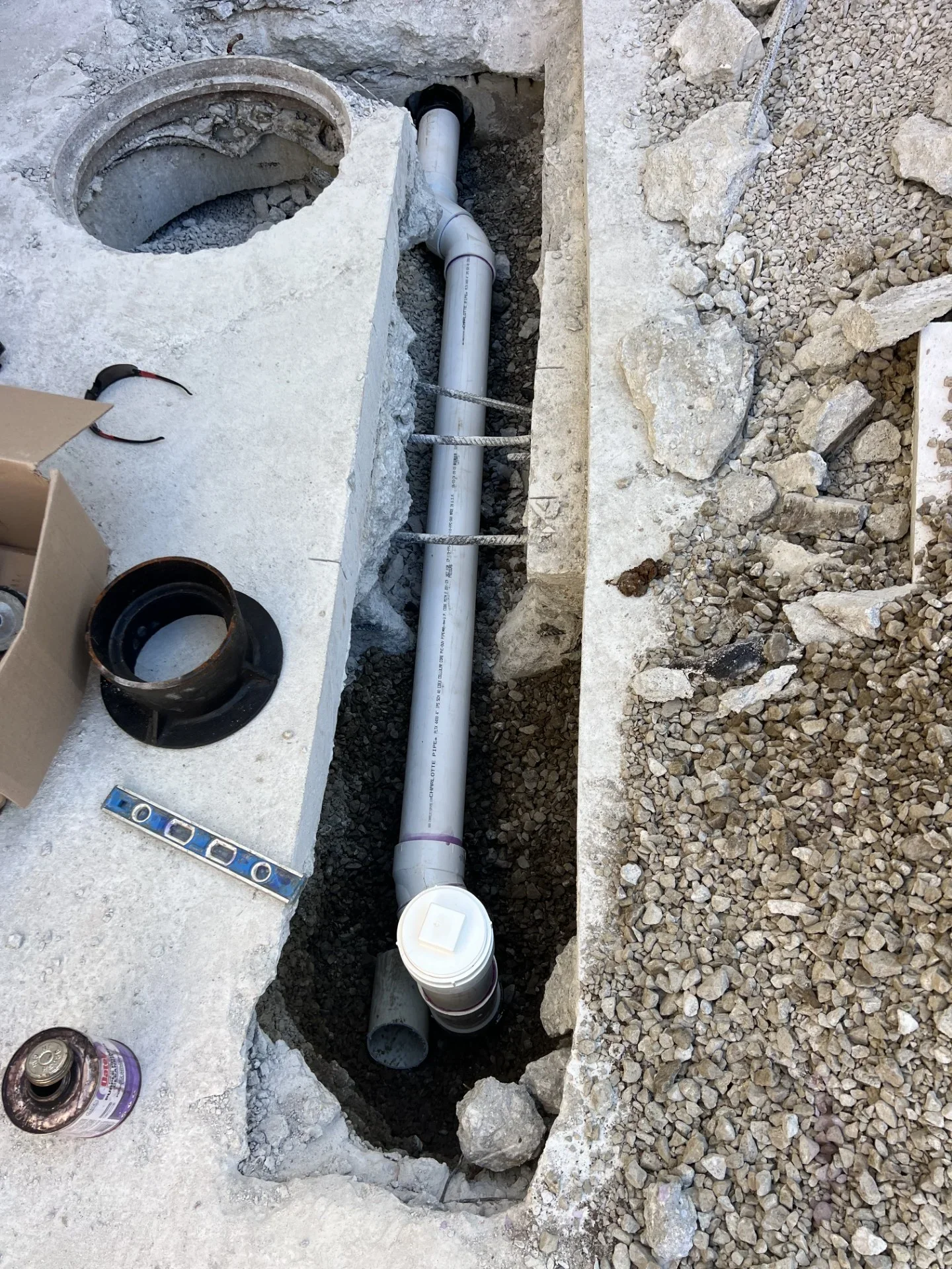 Gray PVC sewer pipe with wye fitting and white cleanout riser in concrete trench with gravel backfill