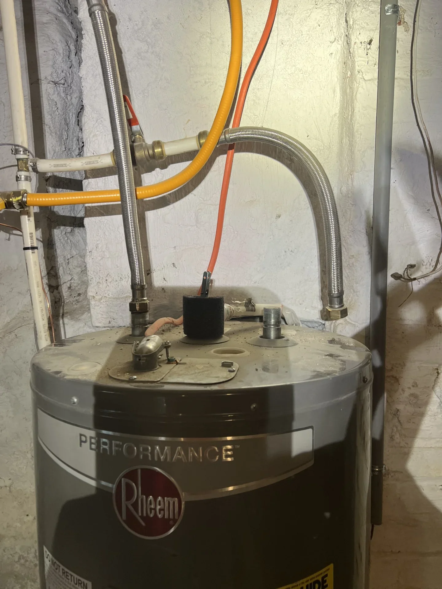 Rheem Performance water heater with stainless steel braided connectors, yellow flexible gas line, and white PVC piping in a basement