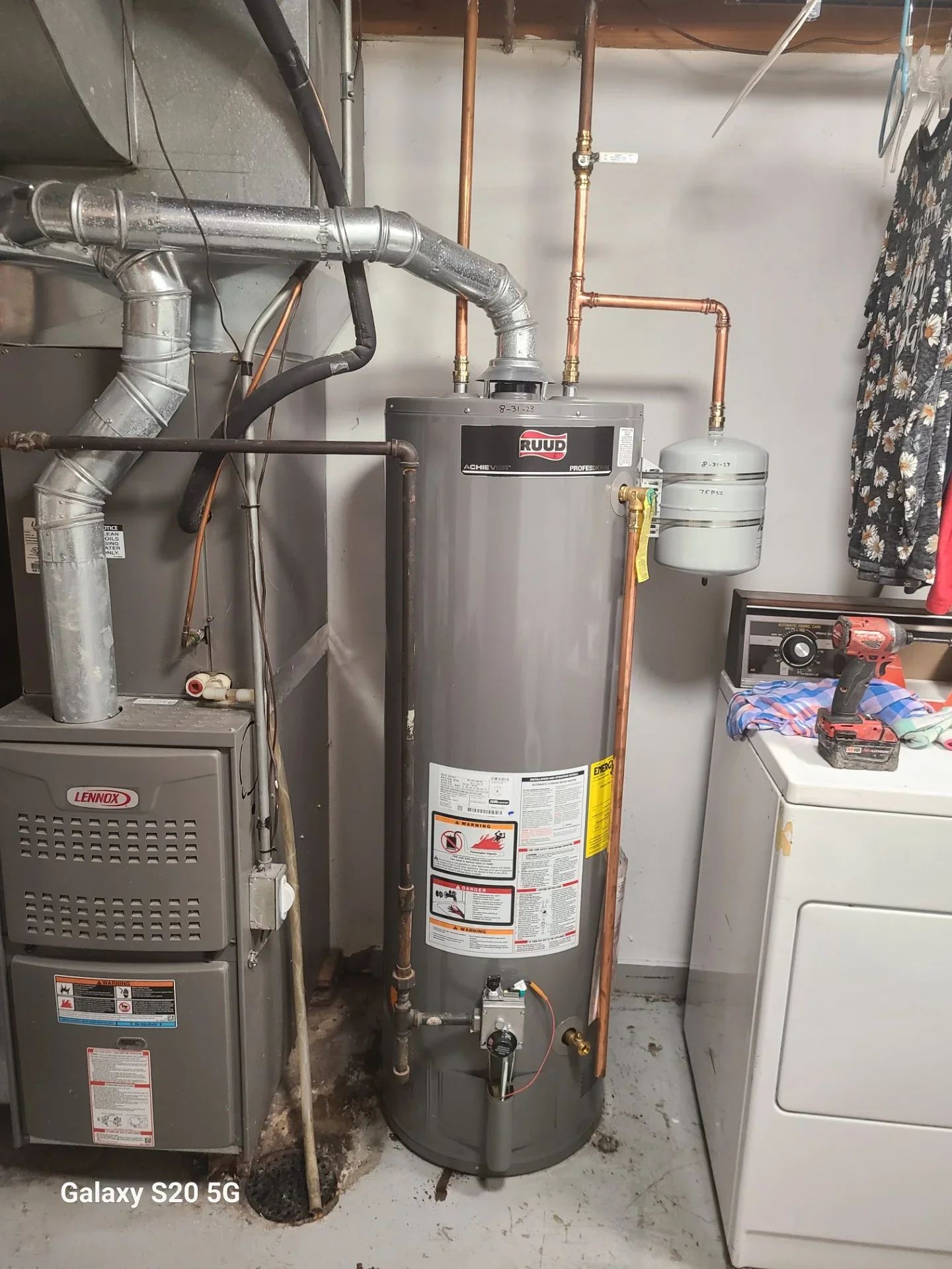 Gray Ruud gas water heater with copper piping, white expansion tank, and galvanized flue vent beside a Lennox furnace