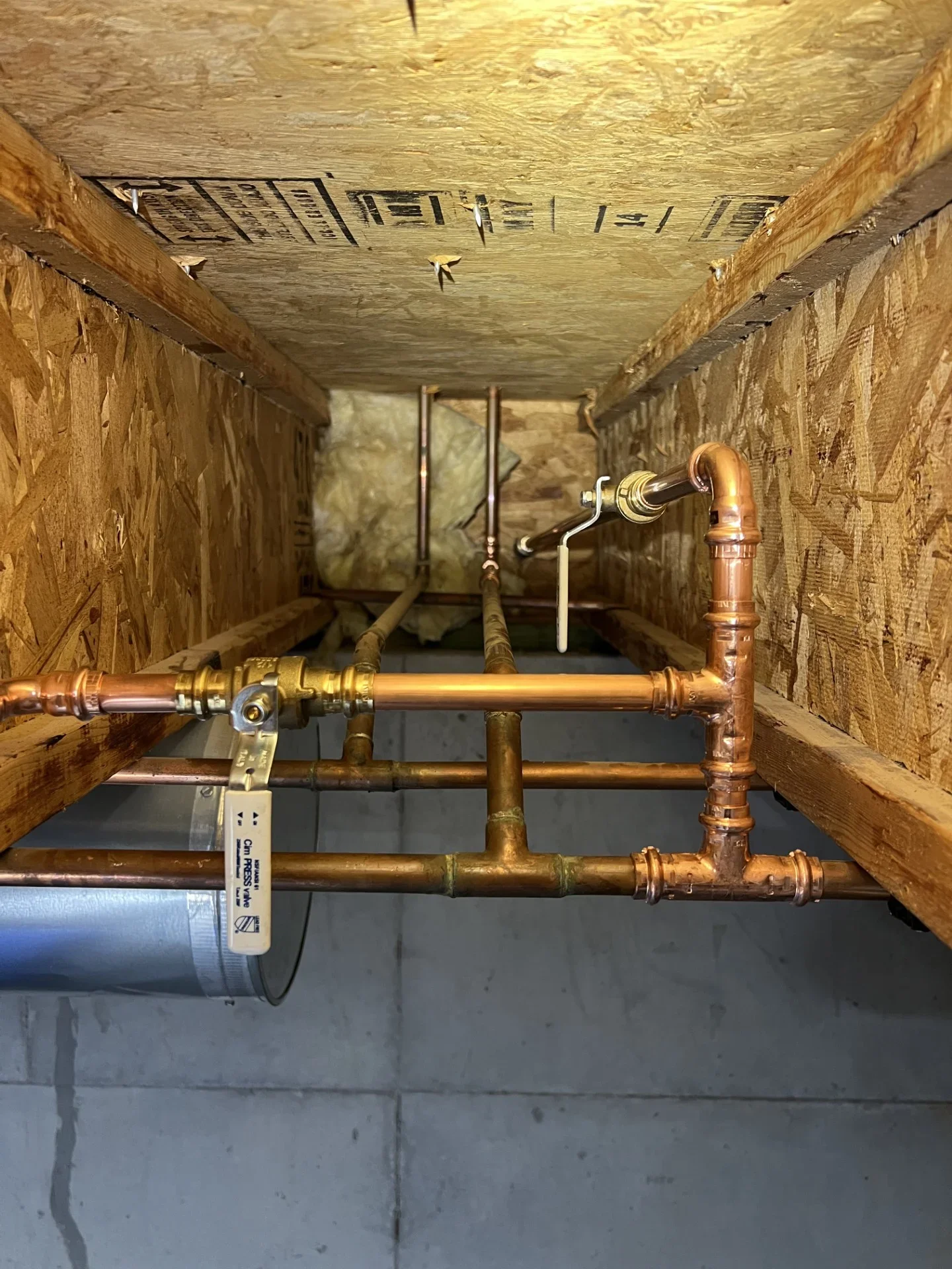 Copper press-fit supply piping with brass ball valve and press fittings routed through an OSB-lined joist bay