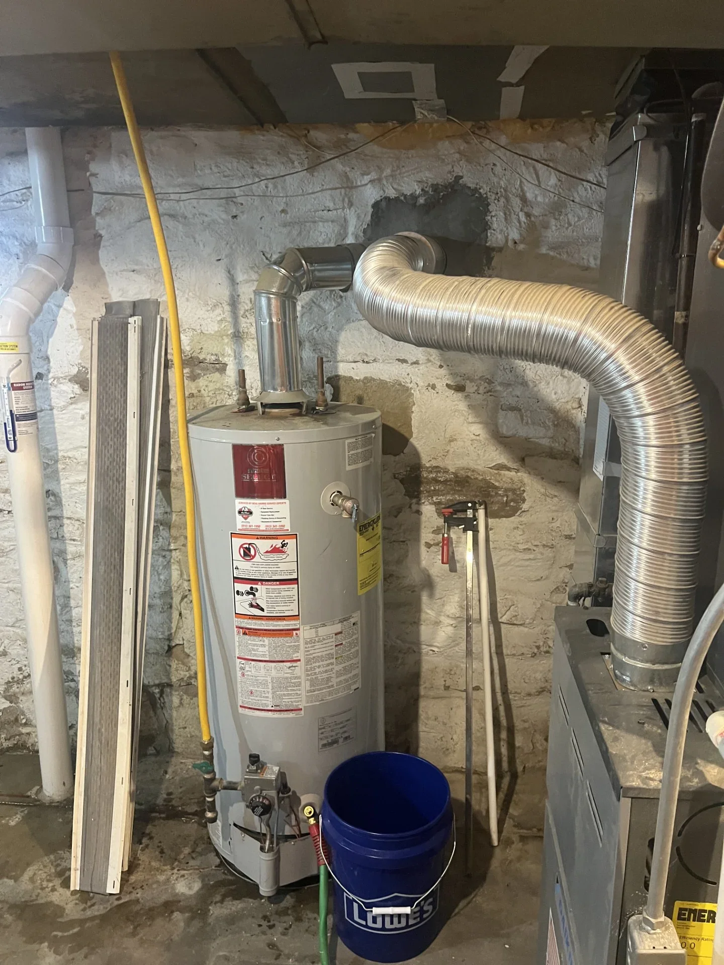Gas water heater with flexible aluminum vent connector and yellow gas line in a basement against a stone wall