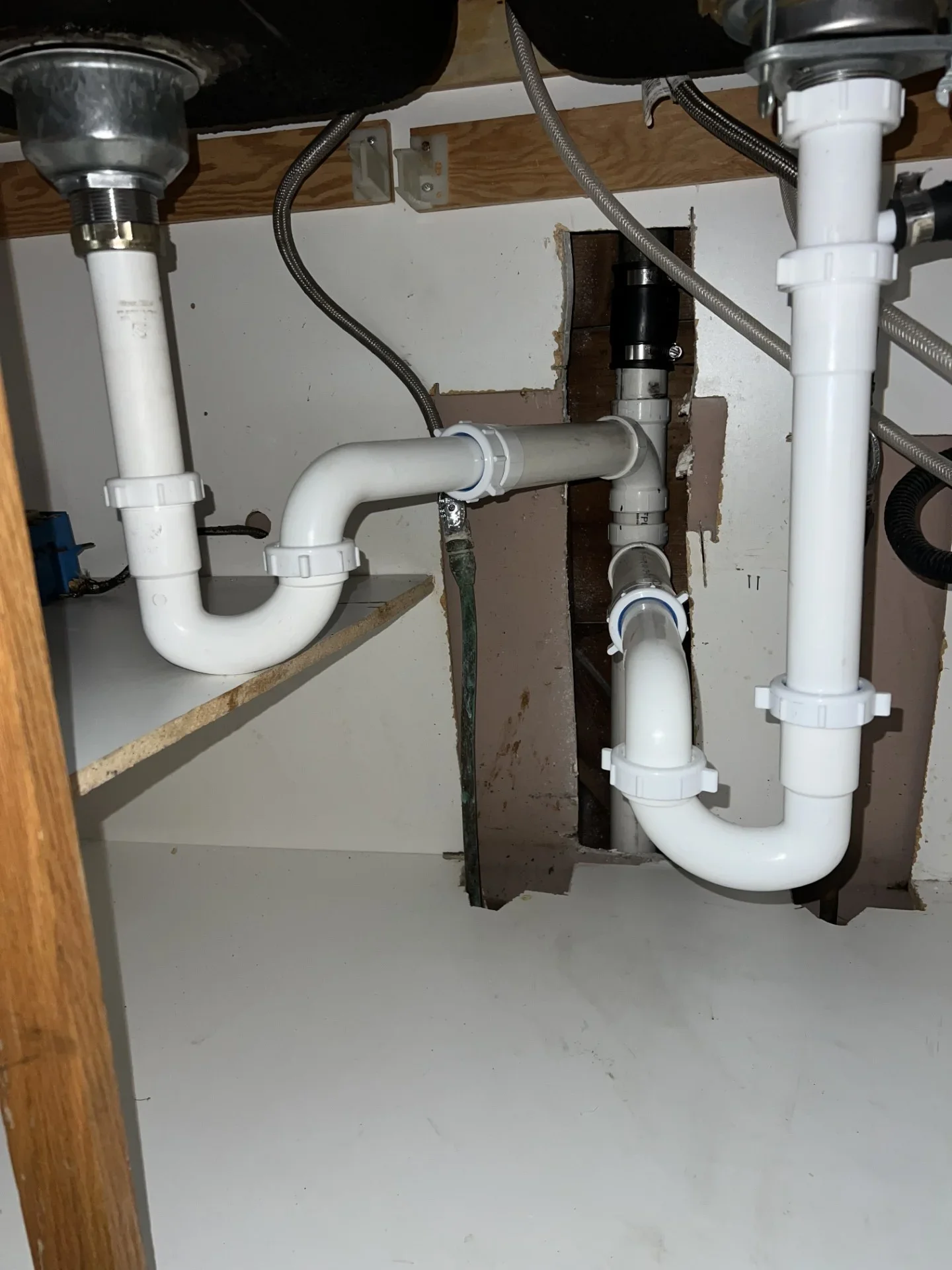 White PVC P-trap drain lines and slip-joint fittings under a double kitchen sink with braided stainless supply lines