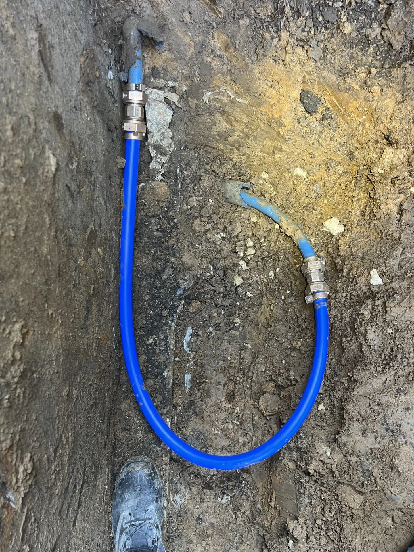 Blue flexible pipe with brass compression fittings installed in an excavated trench during underground line repair