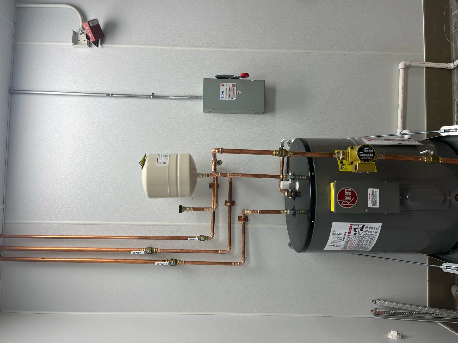 Rheem electric water heater with copper piping, ball valves, white expansion tank, and Eaton disconnect on wall