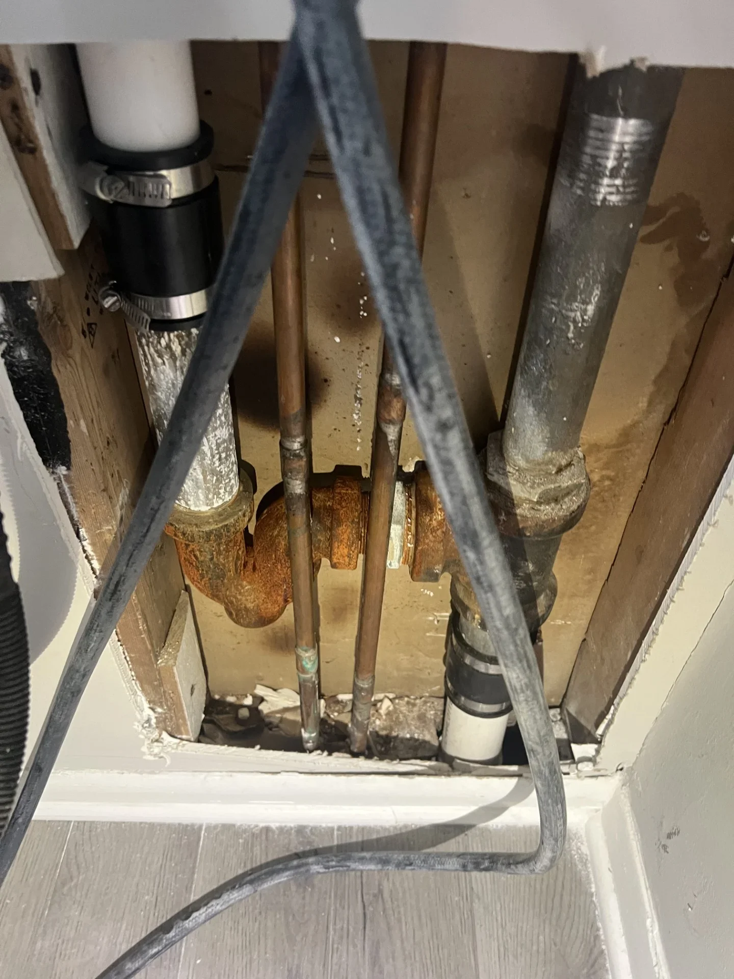 Exposed rusted cast iron P-trap, galvanized steel drain pipe, copper supply lines, and PVC couplings inside an open wall cavity