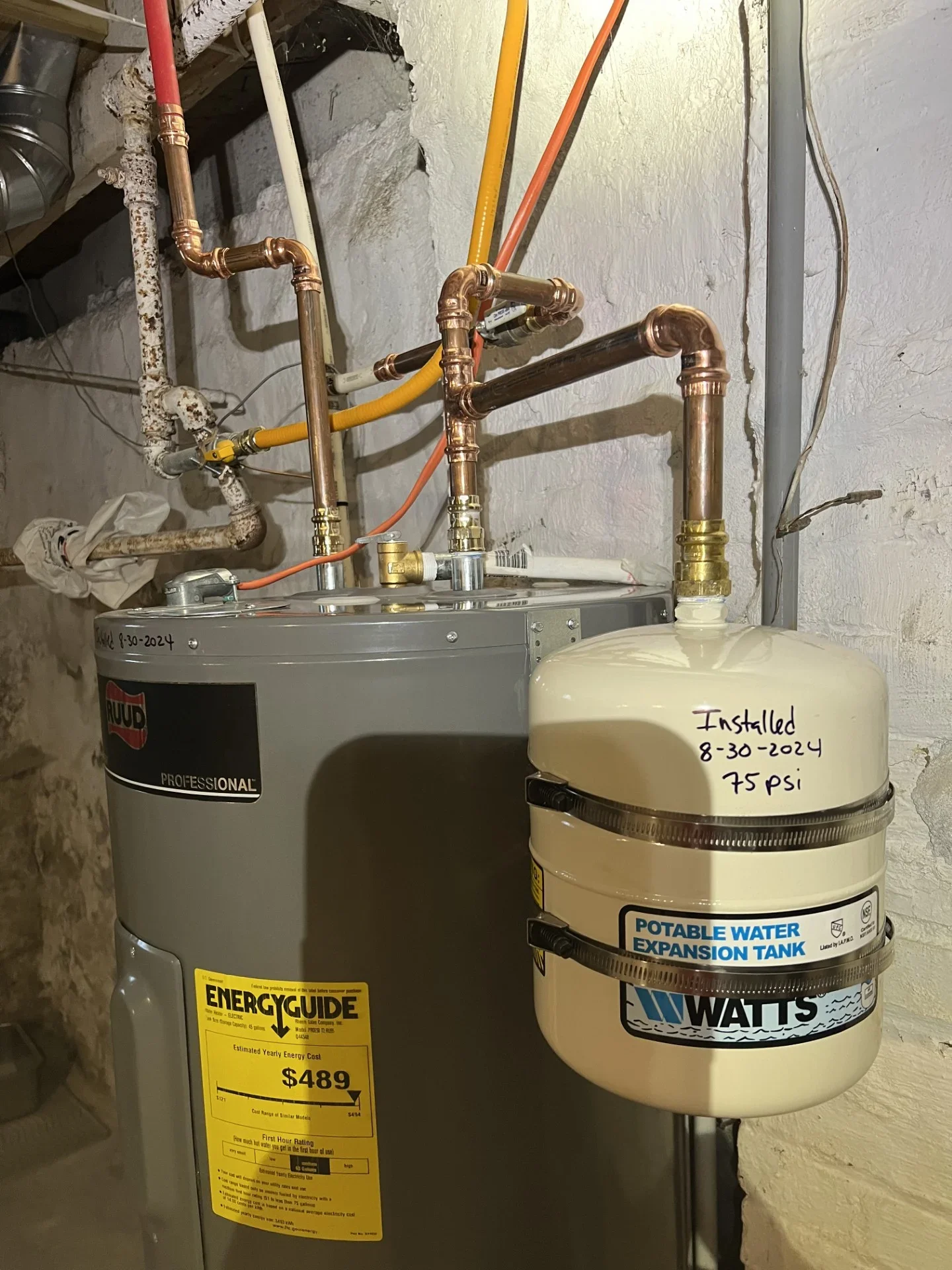 Ruud electric water heater with copper piping, brass fittings, and a Watts potable water expansion tank installed on the cold-water line