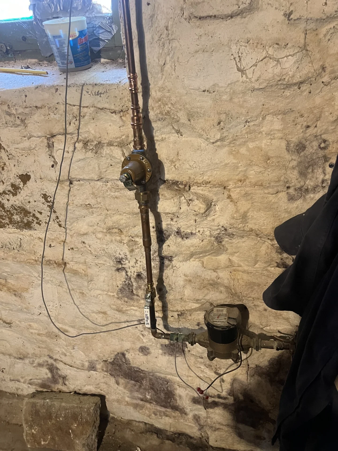 Copper water supply line with brass valves and a utility water meter mounted on a rough stone basement wall
