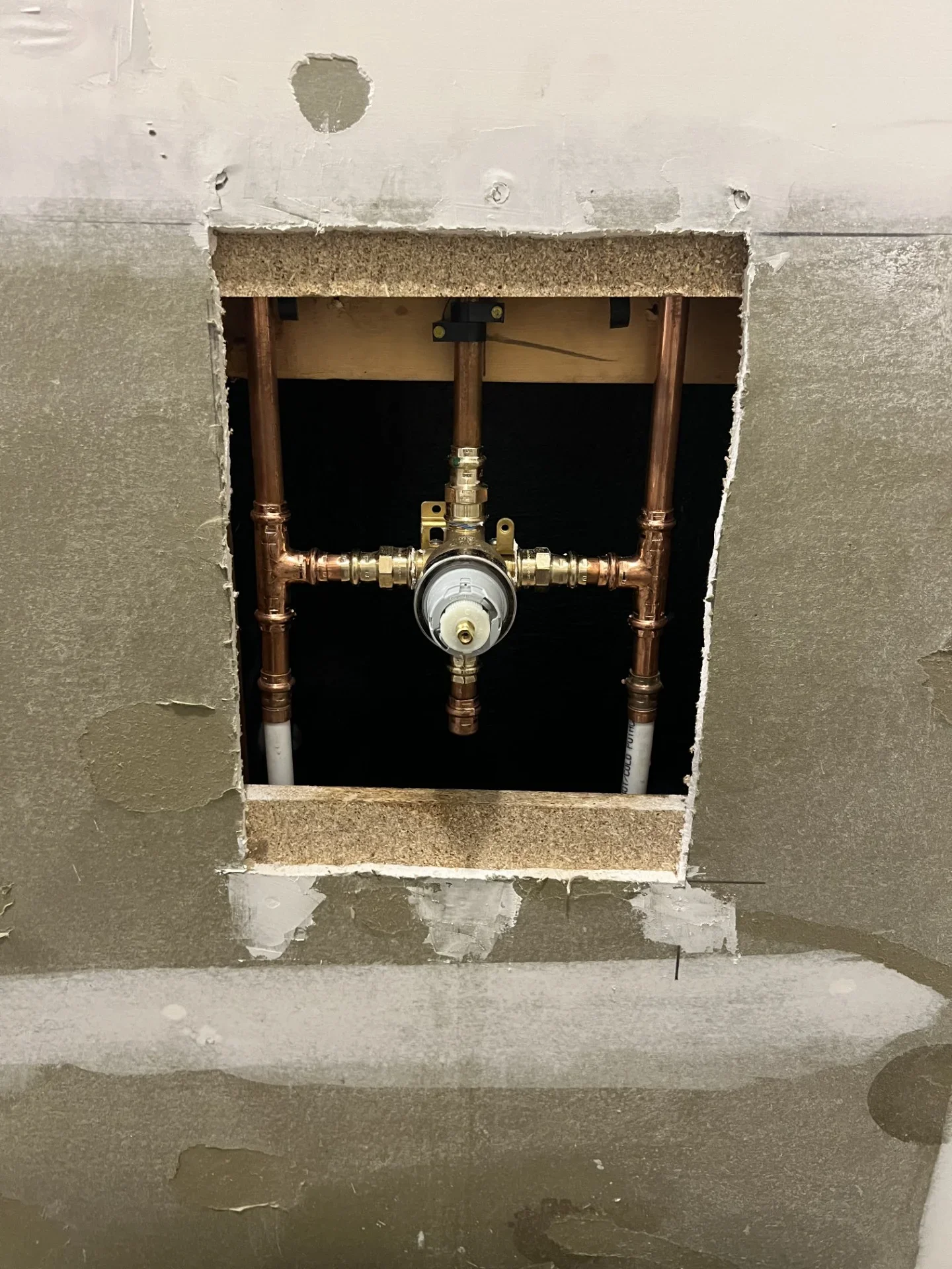 Exposed shower valve rough-in with copper press fittings, brass valve body, and white PEX hot and cold lines behind open drywall