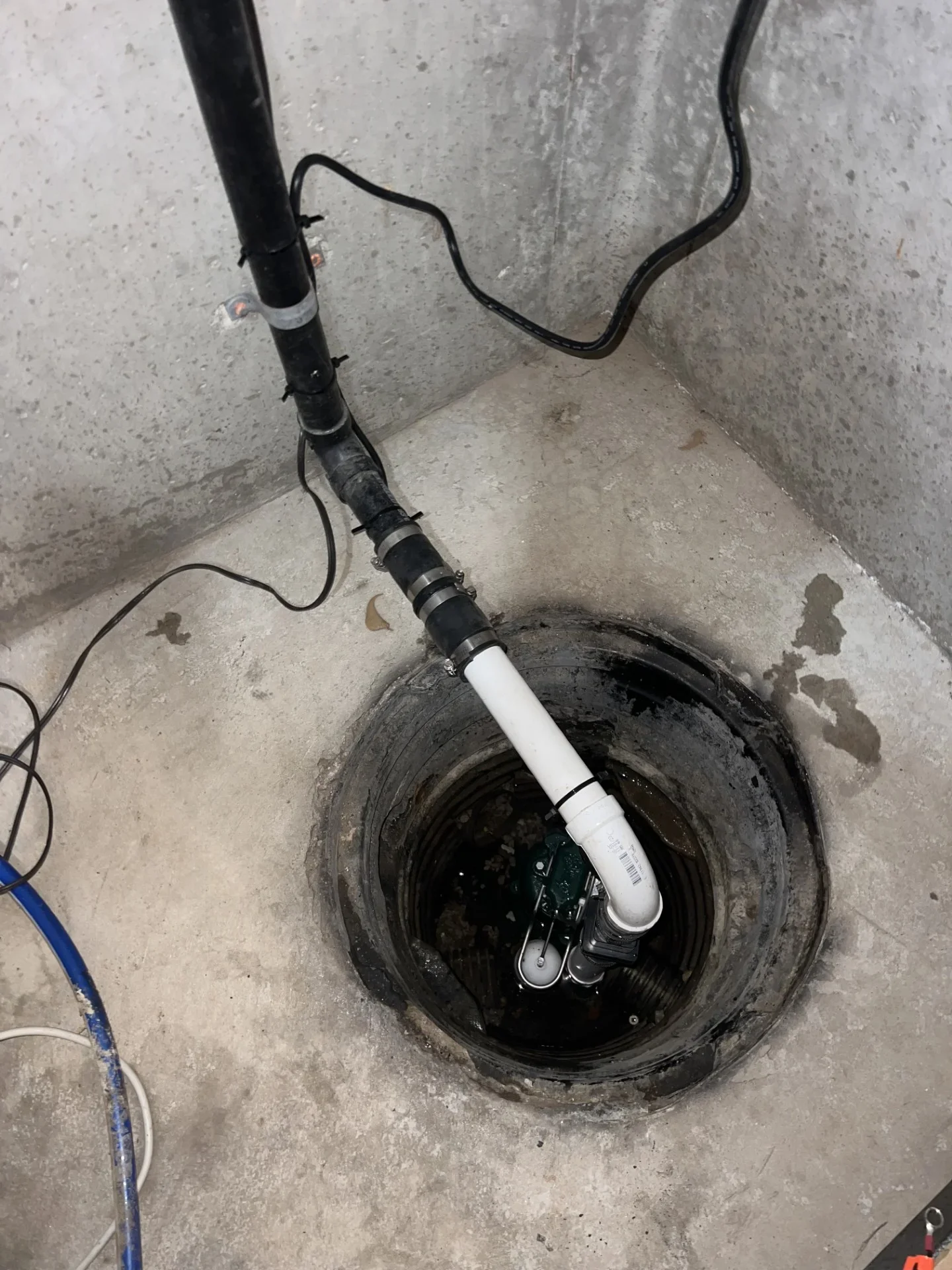 Submersible sump pump with white PVC discharge elbow and black flexible pipe installed in a concrete sump basin